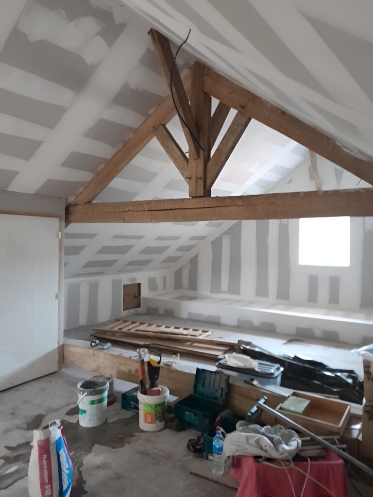 Aménagement de combles avec charpente bois apparente et plaques de plâtre jointoyées en cours de rénovation.