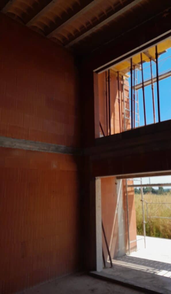 Intérieur d'un chantier : murs en briques rouges, charpente bois et vue sur les échafaudages extérieurs.
