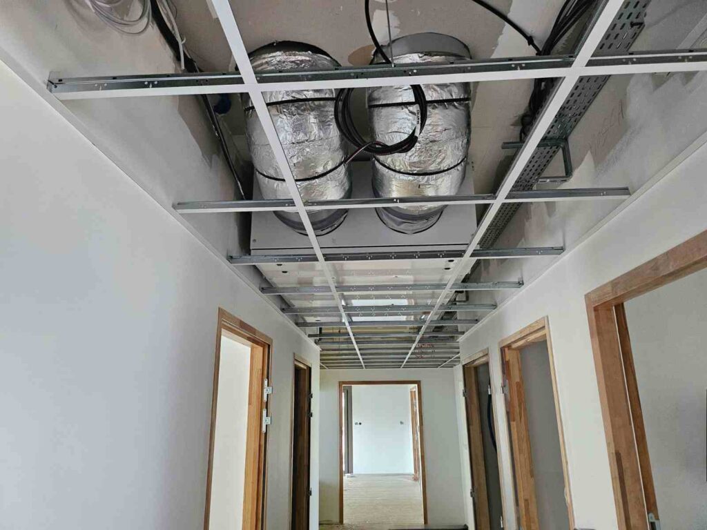 Faux-plafond ouvert montrant gaines de ventilation isolées et câblage électrique dans un couloir en chantier.