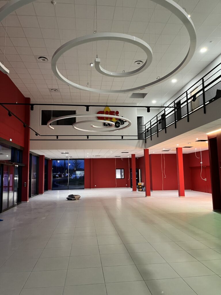 Aménagement intérieur magasin GiFi vide et moderne Magasin GiFi vide, murs rouges, luminaires spirales blancs et mezzanine moderne sur carrelage blanc.