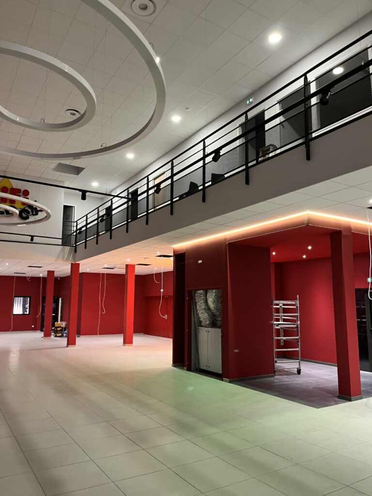Aménagement de local commercial moderne avec murs rouges Local commercial moderne en travaux : murs rouges, mezzanine à rampe noire et éclairages circulaires au plafond.