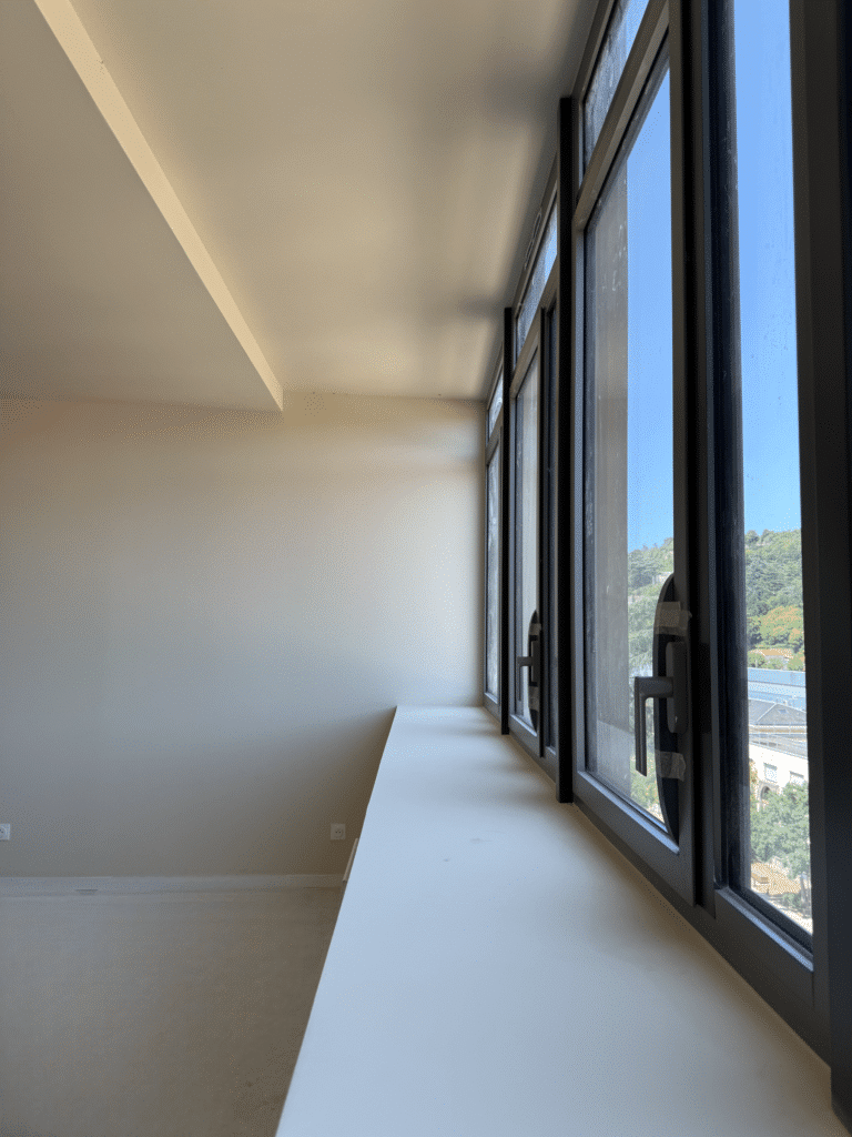 Grandes fenêtres noires dans une pièce blanche minimaliste avec rebord de fenêtre large.
